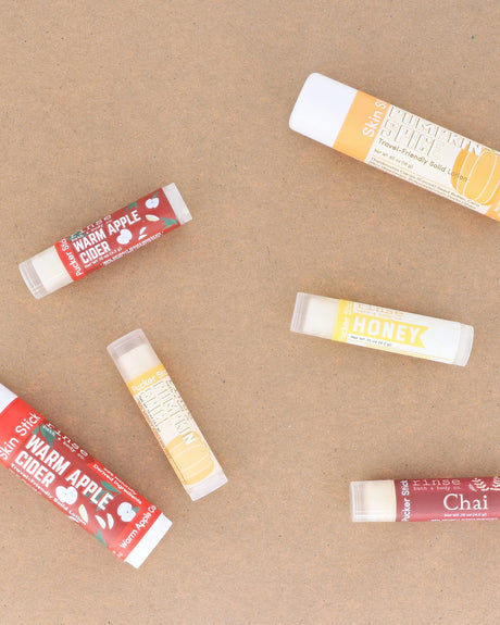 Warm Apple Cider lip balms scattered across warm kraft paper with the season's other flavours — spiced apple, clove and brown sugar for chapped autumn lips. Rinse Bath & Body Co.