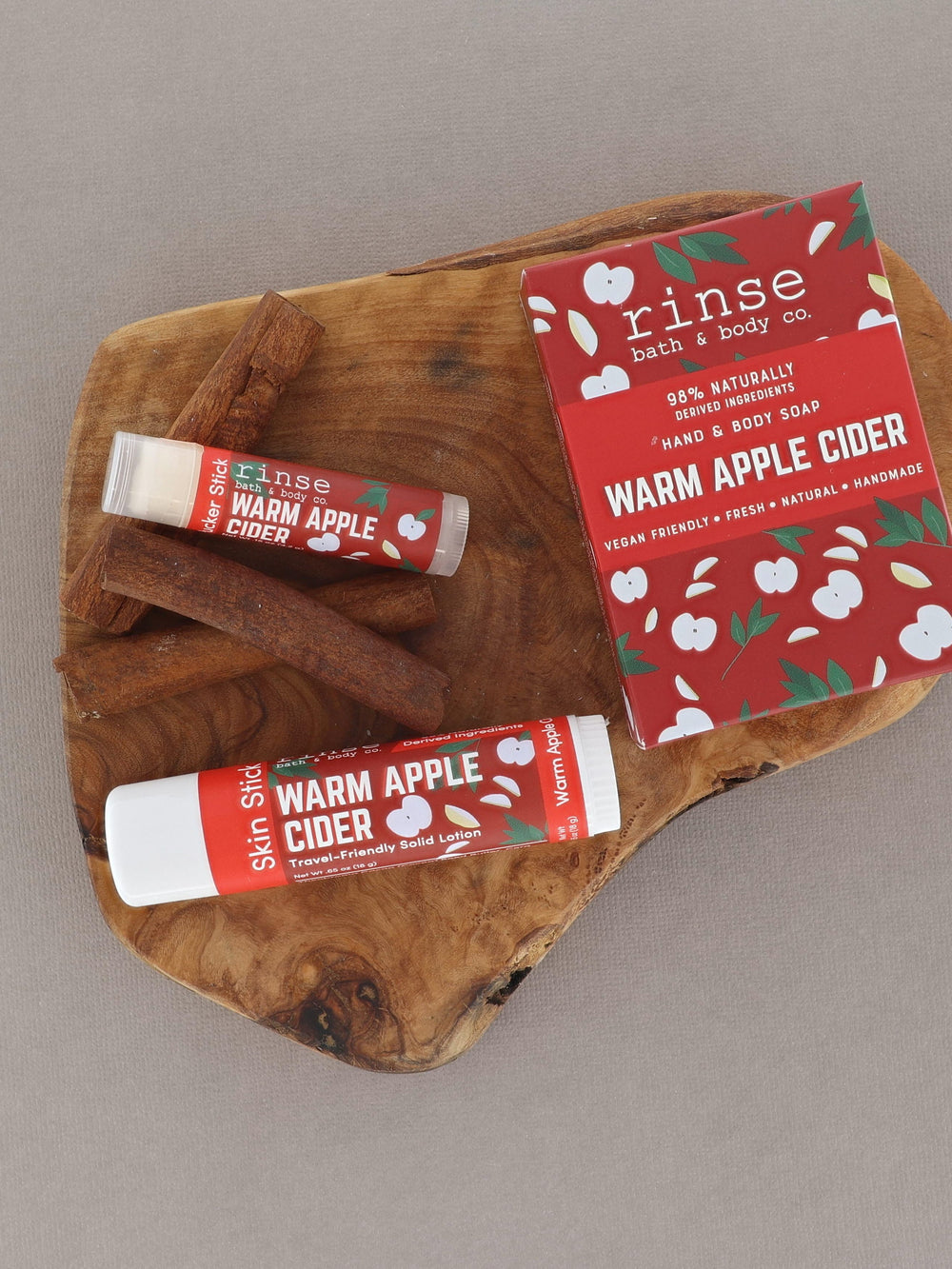 Warm Apple Cider Skin Stick and Pucker Stick on a live-edge wood slice — cinnamon sticks and red apple card on gray