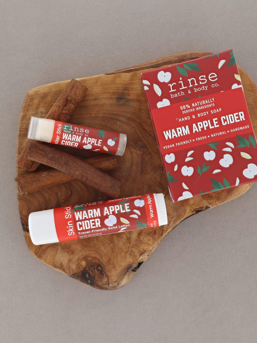 Warm Apple Cider sticks resting with cinnamon on rustic wood — festive red apple packaging on soft gray
