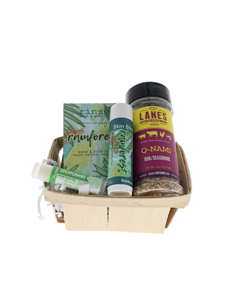 Wooden gift basket packed with Rainforest soap and Skin Stick, Speppermint Pucker, and Lane's BBQ rub against black — leafy greens and spice shaker for a tropical Dad set
