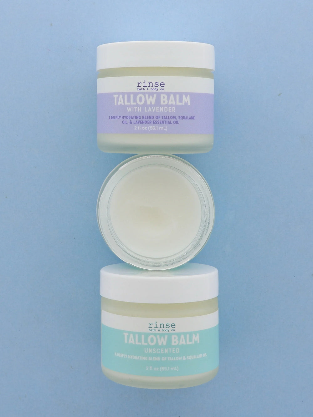 Three tallow balm jars lined on periwinkle blue — lavender, open cream, and unscented teal labels from above