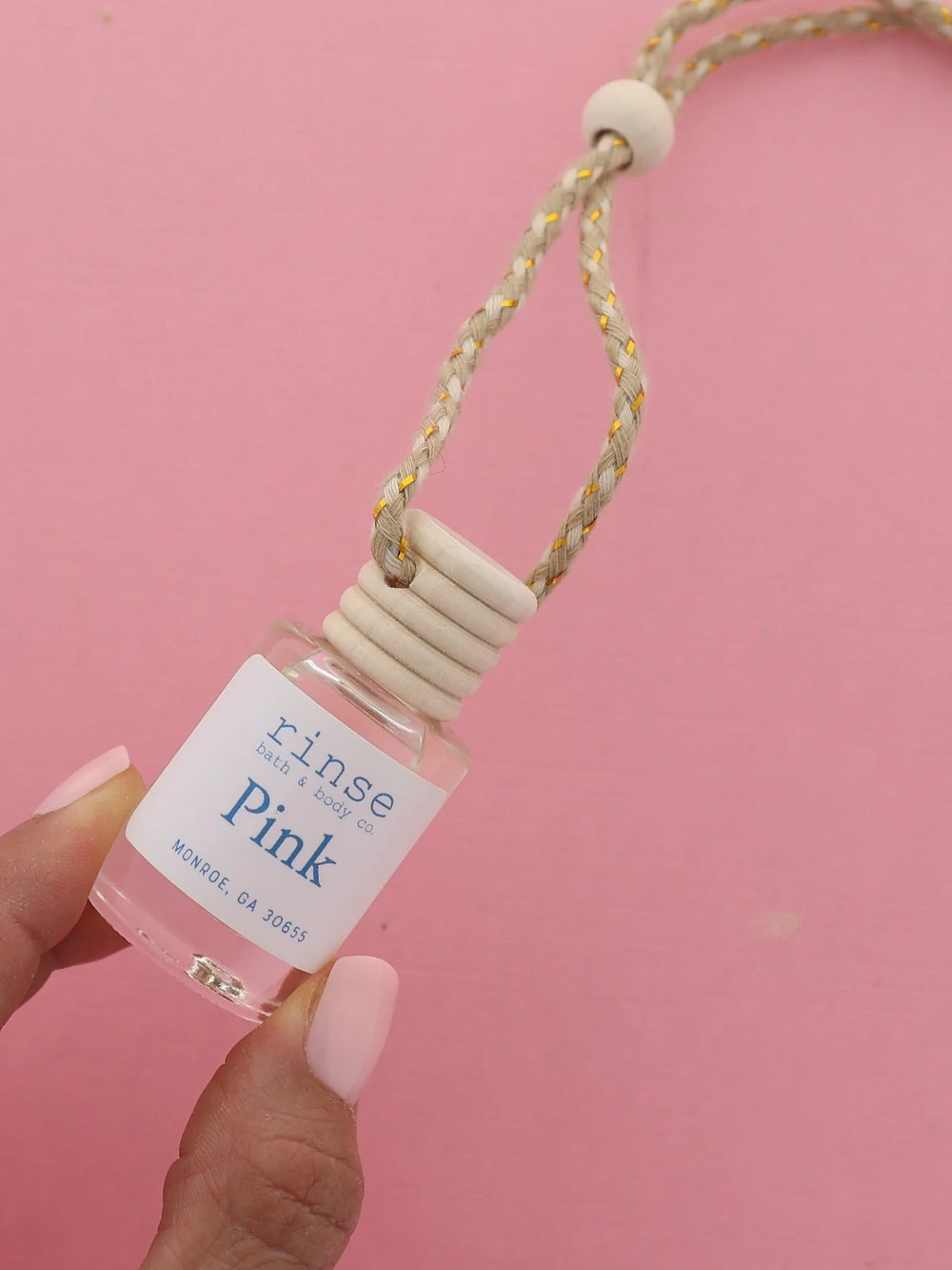 Hand holding Pink car diffuser against saturated pink — wood cap and braided cord in bold studio light