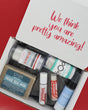 An open white gift box filled with bath and body items, photographed from above on a red background. The inside lid reads 'We think you are pretty amazing!' in pink script.