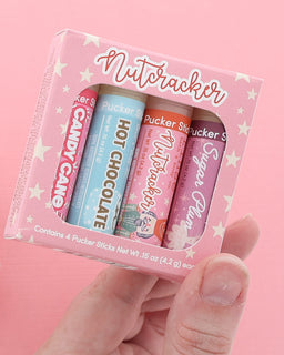 Hand holding the Nutcracker lip balm four-pack with Candy Cane, Hot Chocolate, Nutcracker and Sugar Plum sticks on pink