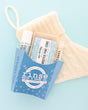 Frosted Pine Cone gift set in a blue fry carton with soap, Skin Stick and Pucker Stick beside a cream knit stocking