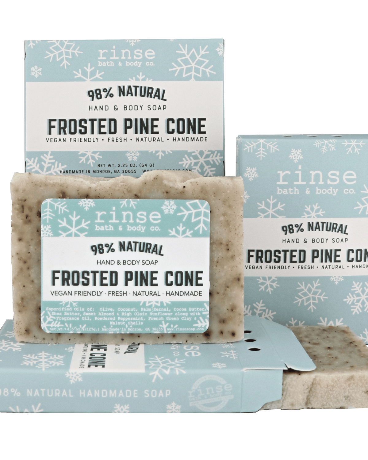 Mini Frosted Pine Cone soap standing before snowflake cartons on forest green — speckled cream bar in crisp winter light