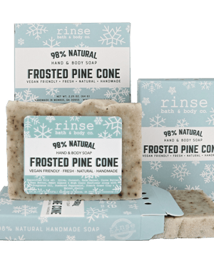 Mini Frosted Pine Cone soap standing before snowflake cartons on forest green — speckled cream bar in crisp winter light