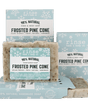 Mini Frosted Pine Cone soap standing before snowflake cartons on forest green — speckled cream bar in crisp winter light