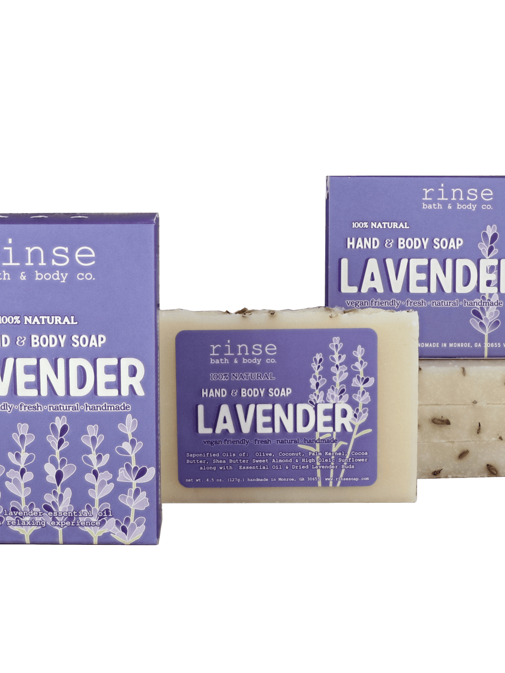 Two purple Lavender soap boxes and a flecked cream bar resting on deep green — botanical buds catching soft studio light