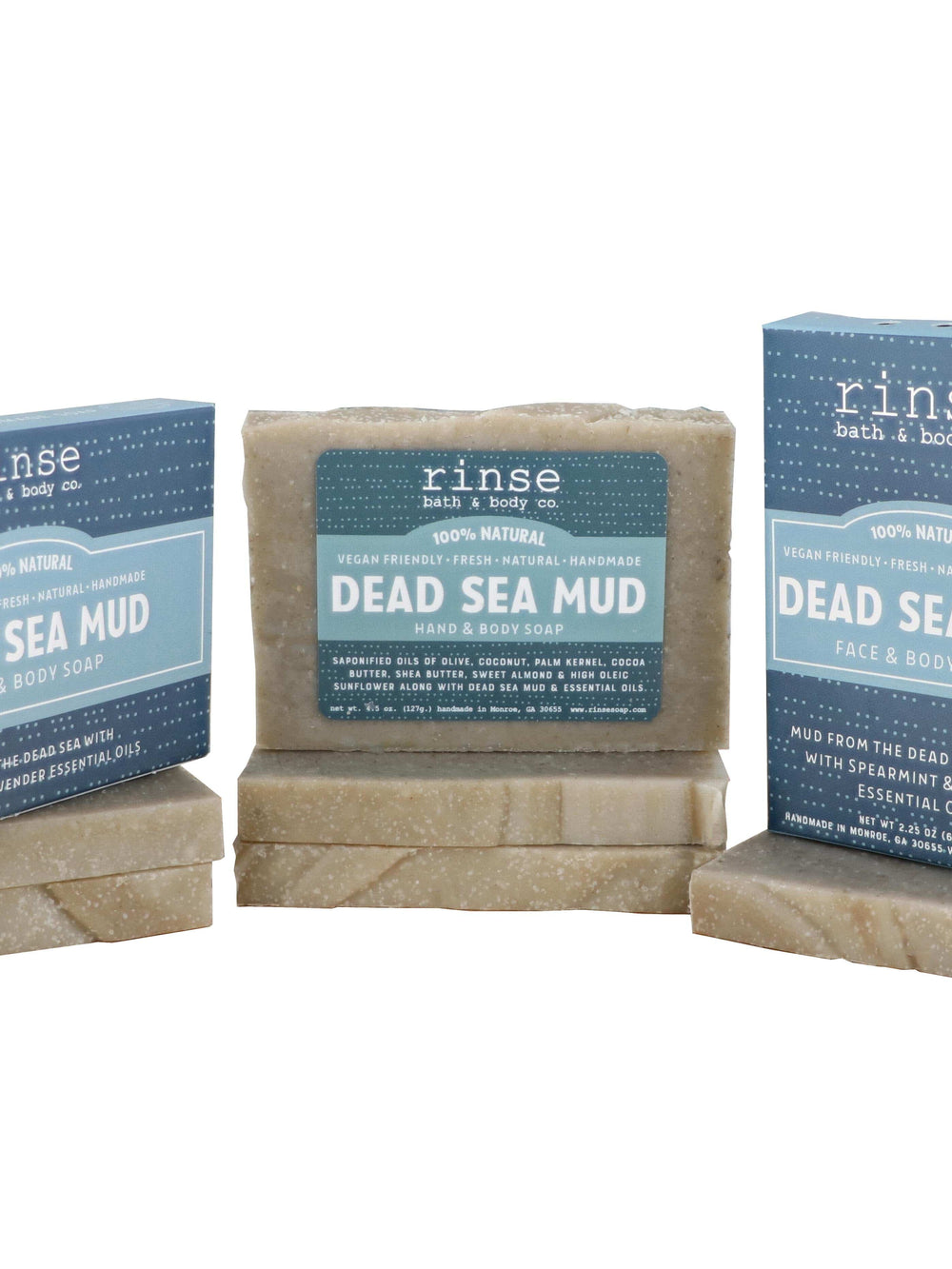 Dead Sea Mud bars and dotted blue boxes stacked on clean white — grainy mineral soap catching bright studio light