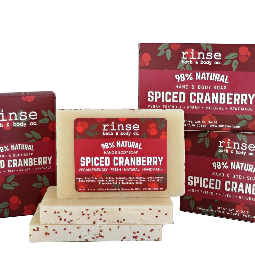 Mini Spiced Cranberry soaps stacked before burgundy cartons on weathered wood — seed-flecked cream bars