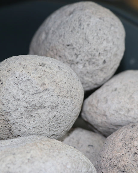 Coarse light grey pumice stones pile in a dark bowl — porous pitted volcanic texture in soft focus