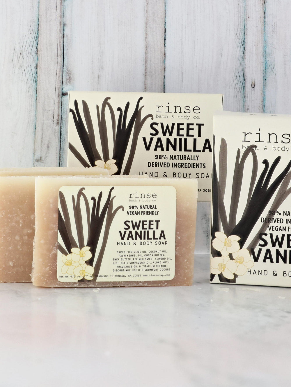 Sweet Vanilla mini soaps and white cartons on marble — blue-washed wood planks glowing behind