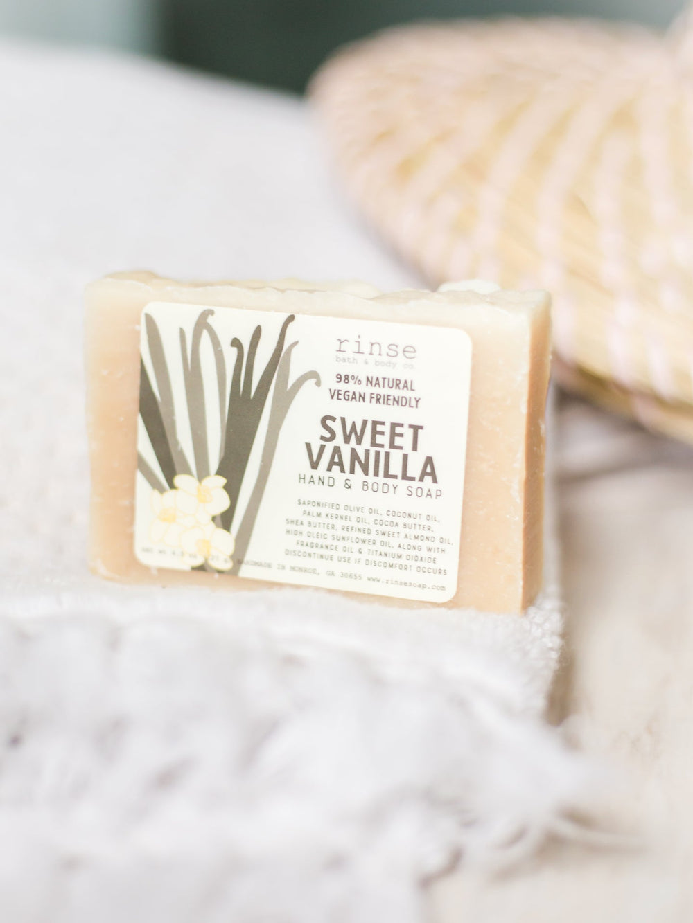 Sweet Vanilla mini soap resting on a white fringe towel — soft sunlit blur of woven basket behind