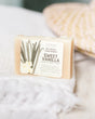 Sweet Vanilla mini soap resting on a white fringe towel — soft sunlit blur of woven basket behind