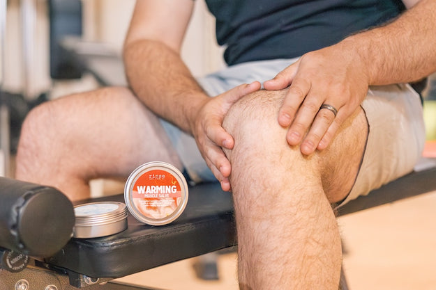 man applying warming muscle salve to leg after a workout at the gym