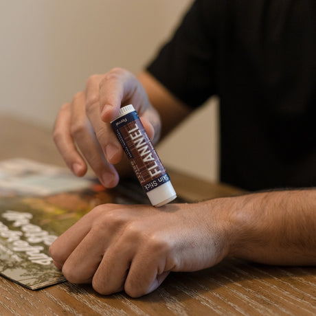 A man working Flannel solid lotion into the back of his hand at a desk — mess-free hydration with a warm woodsmoke finish, from the Flannel fry-box gift set. Rinse Bath & Body Co.