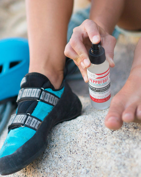 Peppofoot Refreshing Spray being misted onto a bare foot on a rock, a blue climbing helmet and shoe beside it