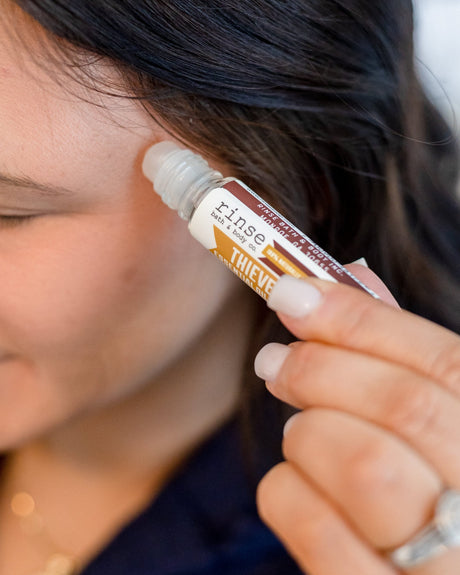 Thievery essential oil roll-on applied to the temple — the warm four-thieves blend of clove, cinnamon, lemon, rosemary and eucalyptus on a squalane base. Rinse Bath & Body Co.
