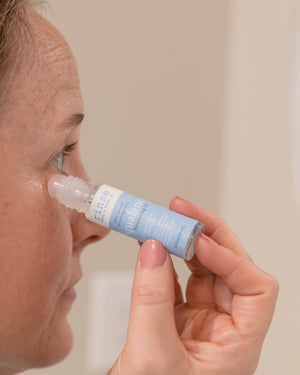A woman rolling Squalane oil along her under-eye with the glass rollerball