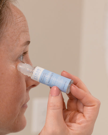 A woman rolling Squalane oil along her under-eye with the glass rollerball