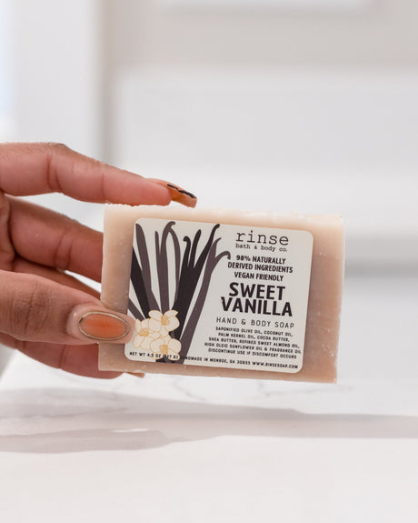 Sweet Vanilla bar soap in use, worked into a creamy lather — warm bourbon vanilla over a cocoa-butter base. Rinse Bath & Body Co.