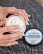 Two hands twisting open a jar of Blue Hawaiian Body Spread, blue label facing the camera