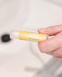 Ginger Lemongrass lip balm held in soft daylight — sharp ginger and bright lemongrass in a cocoa-butter balm. Rinse Bath & Body Co.