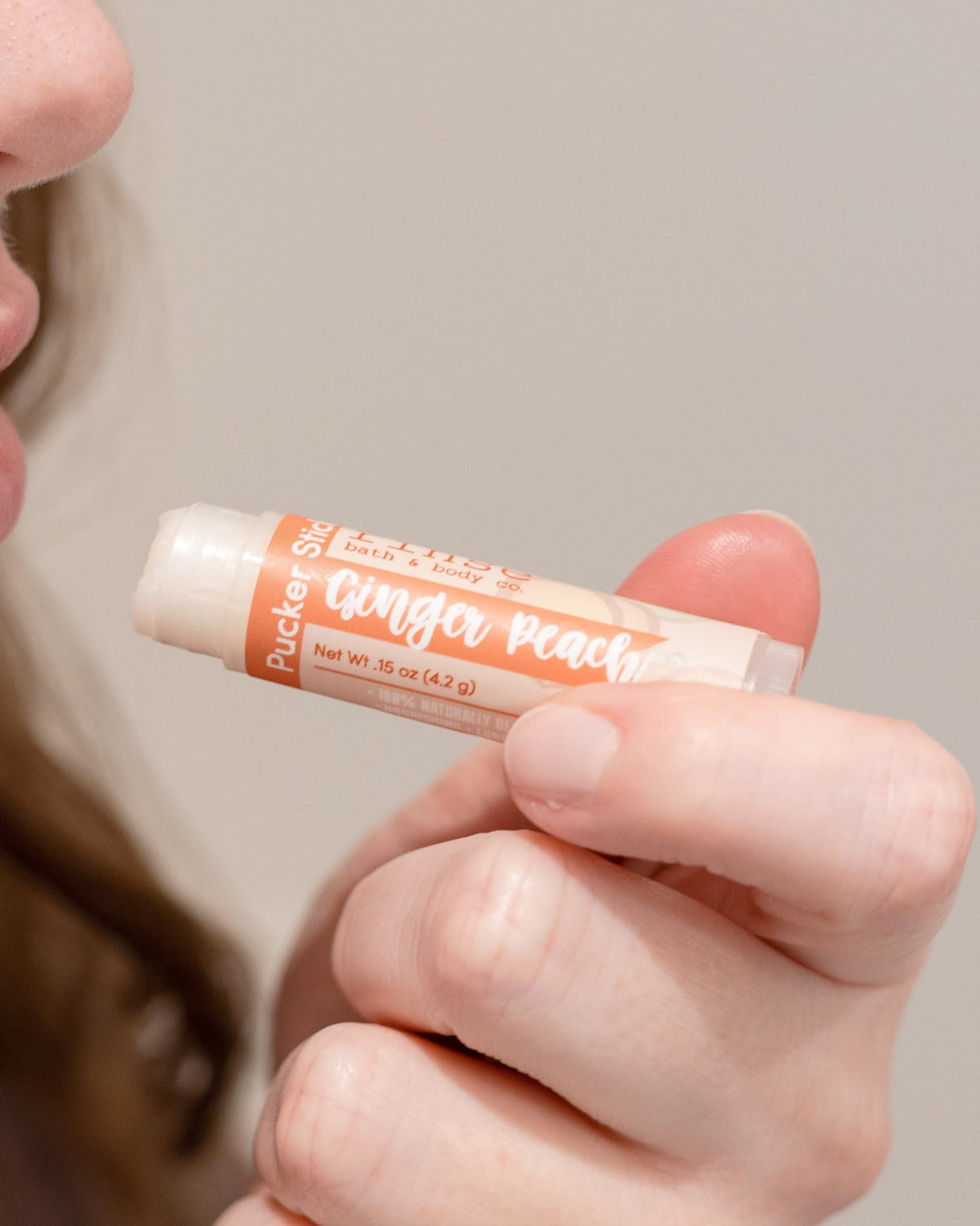 Ginger Peach Pucker Stick in hand with the cap off — a twist-up balm that softens without a waxy film. Rinse Bath & Body Co.