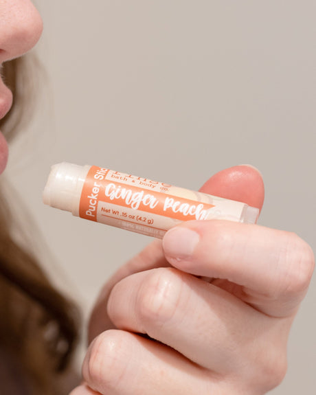 Ginger Peach Pucker Stick in hand with the cap off — a twist-up balm that softens without a waxy film. Rinse Bath & Body Co.