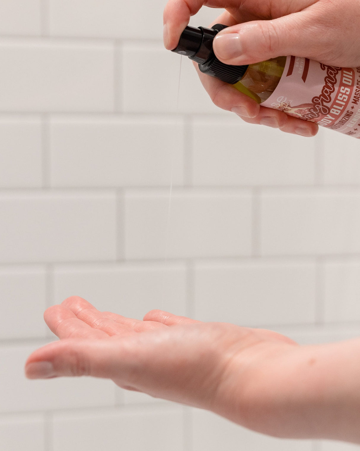 Pomegranate Body Bliss oil in use, smoothed down the arm — a lightweight oil that leaves a soft sheen and sinks in fast. Rinse Bath & Body Co.