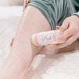 A hand gliding a Pink Skin Stick along a bare leg, the twist-up solid lotion applied straight to the skin — waterless butter-rich moisture, no bottle. Rinse Bath & Body Co.