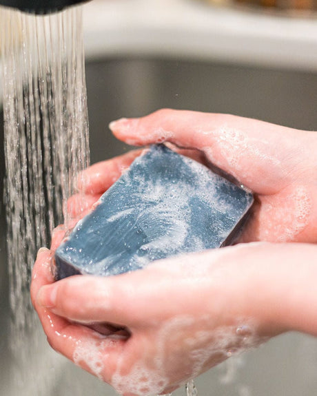 Hands lathering the marbled navy Flannel bar under running water