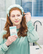 A woman in a headband applying Yogurt Face Mask at the bathroom mirror. Rinse Bath & Body Co.