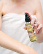 Thievery Body Bliss oil in use, smoothed into skin after a shower — clove and cinnamon warmth that sinks straight in. Rinse Bath & Body Co.