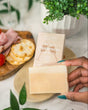 Hand holding Champagne soap beside charcuterie and greenery in bright daylight — bubbly sparkling notes for a festive rinse