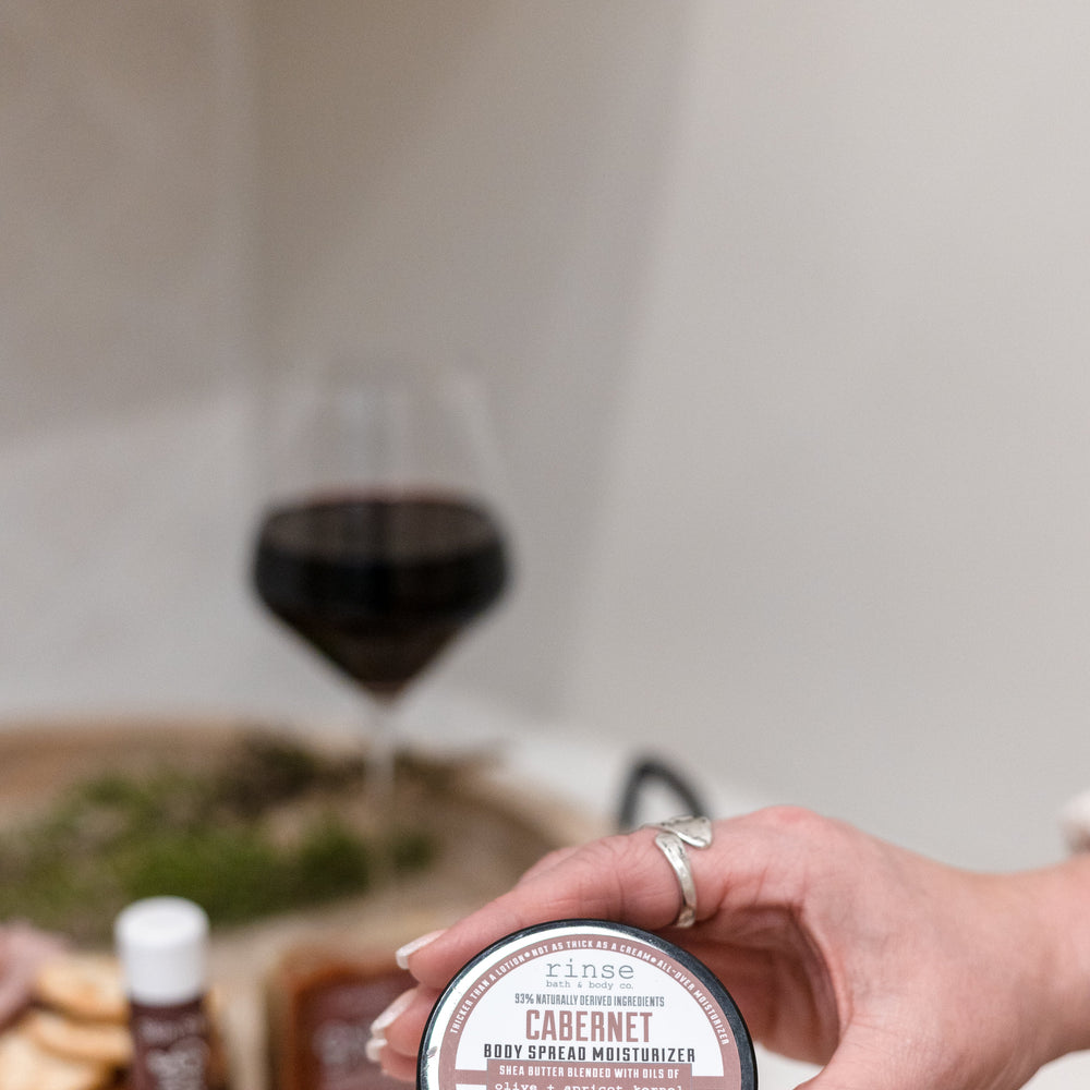 Cabernet body spread scooped from the tub and worked into skin — a thick shea-butter moisturizer carrying deep red wine and dark berry. Rinse Bath & Body Co.