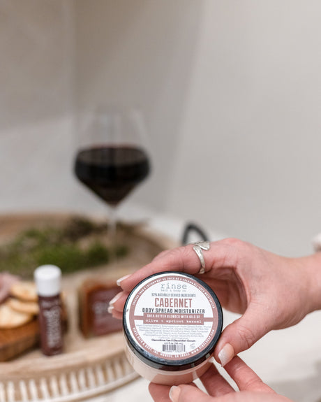 Cabernet body spread scooped from the tub and worked into skin — a thick shea-butter moisturizer carrying deep red wine and dark berry. Rinse Bath & Body Co.