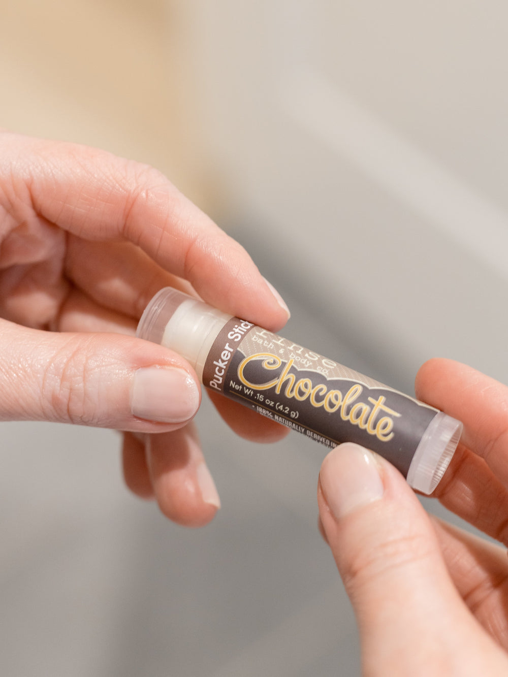 Chocolate lip balm in use, the tube held up to the light — cocoa butter and shea for dry, chapped lips. Rinse Bath & Body Co.