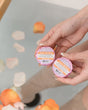 Two hands holding Coco Kissed Tub Truffles above a bath scattered with flower petals — three cocoa butter baths, boxed and ready to give. Rinse Bath & Body Co.
