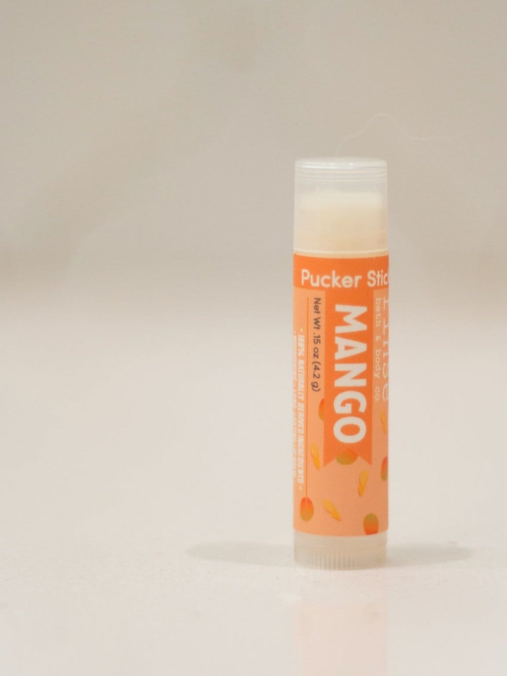 Mango Pucker Stick standing upright in clean studio light — saturated orange label with mango illustrations and translucent cap