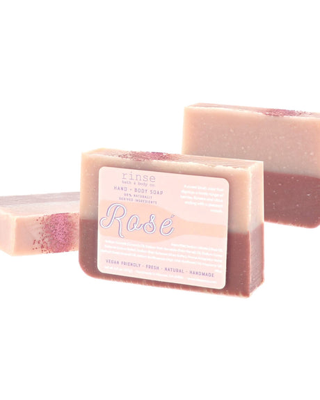 Rosé soap with cream-over-blush layers stands front — pale pink script label on clean bright white