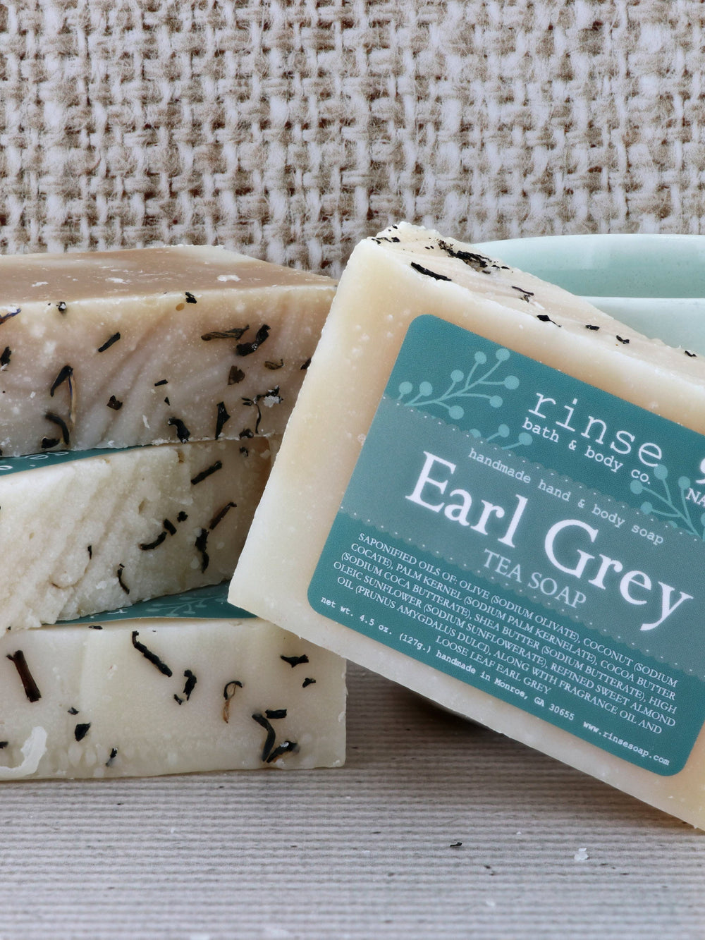 Earl Grey Tea Soap stack on coarse burlap — tea-flecked cream bars with teal label in warm light