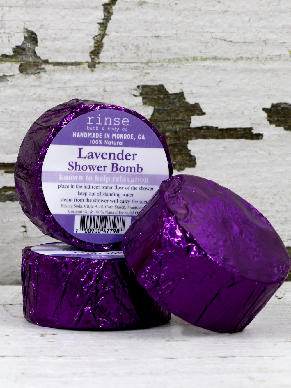 Purple-foil Lavender Shower Bombs stack on peeling white wood — metallic wrap catching rustic light
