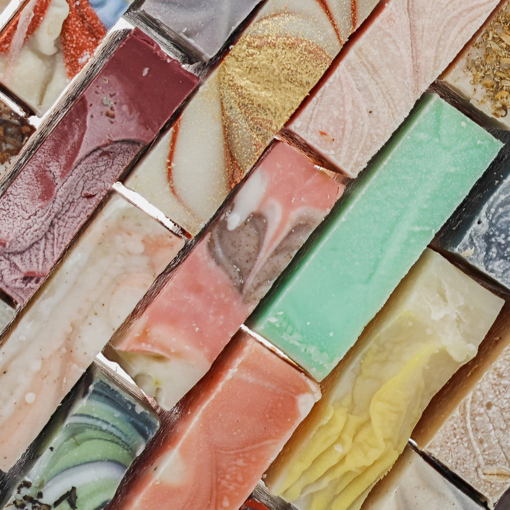 Colorful handmade soap bars line up in diagonal rows — pink sage yellow charcoal swirls in soft light