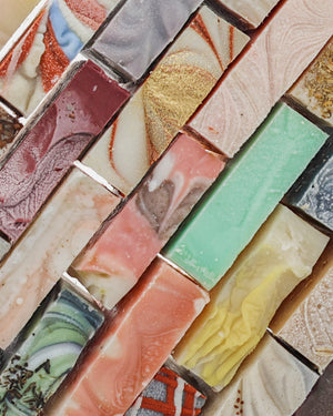 Colorful handmade soap bars line up in diagonal rows — pink sage yellow charcoal swirls in soft light