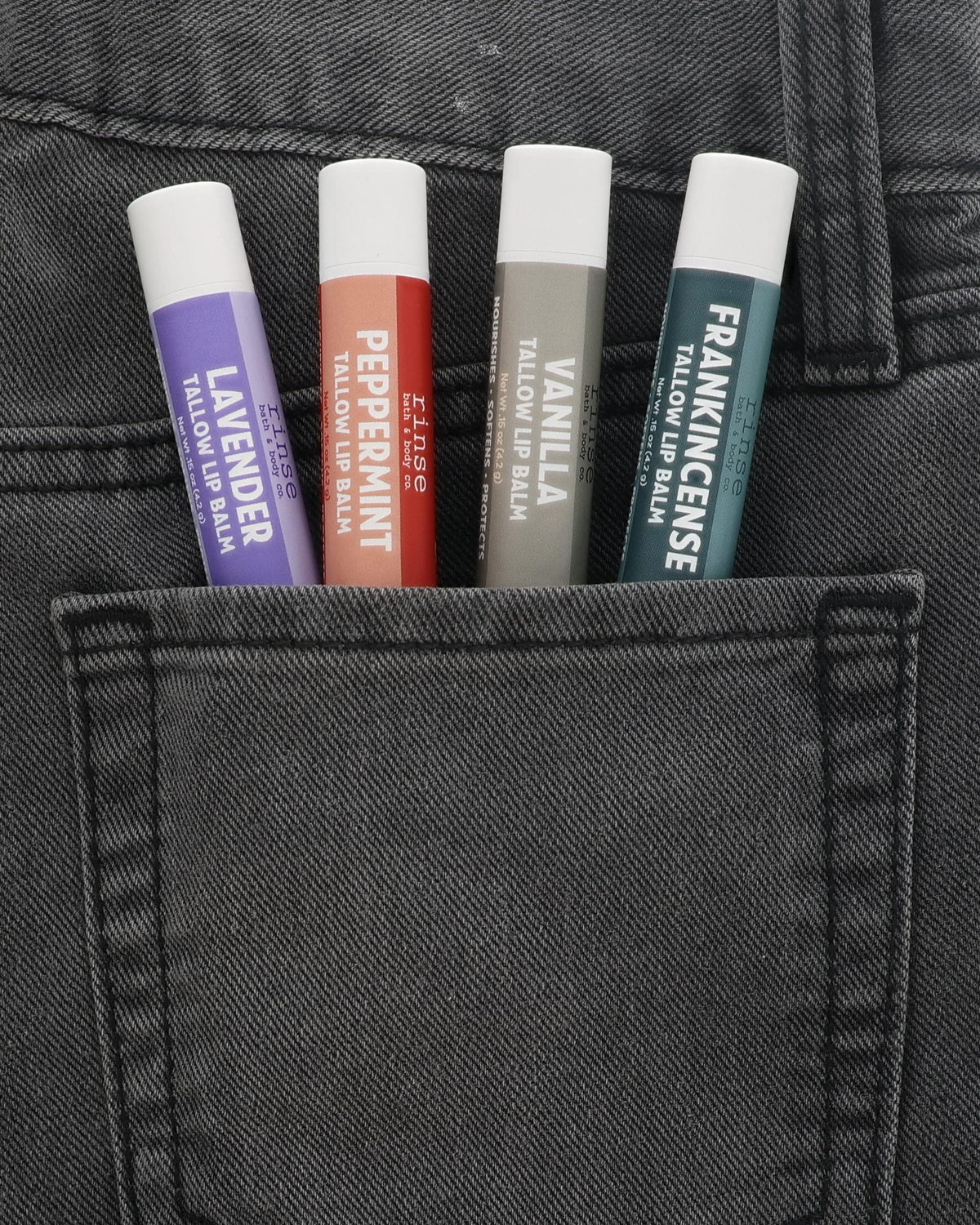Lavender, Peppermint, Vanilla and Frankincense Tallow Lip Balms tucked side by side in a charcoal jeans back pocket