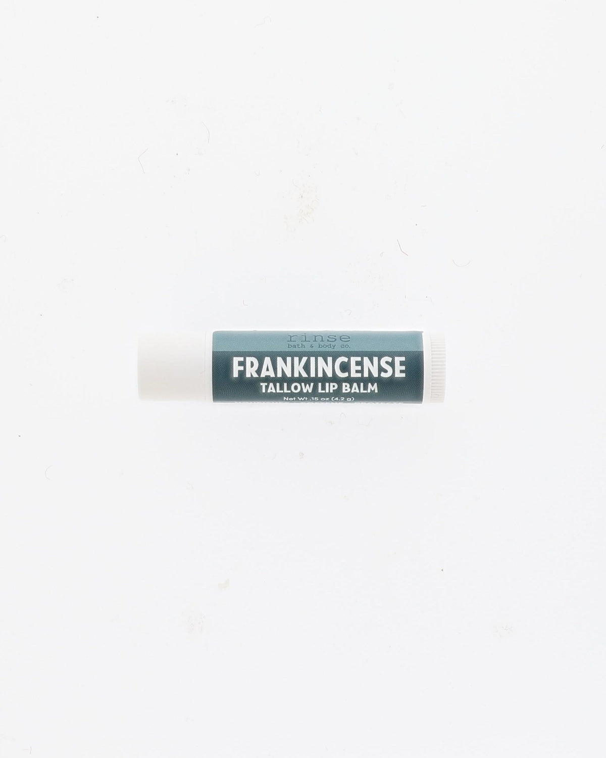 Frankincense Tallow Lip Balm tube with deep teal label and white cap lying on a plain white background
