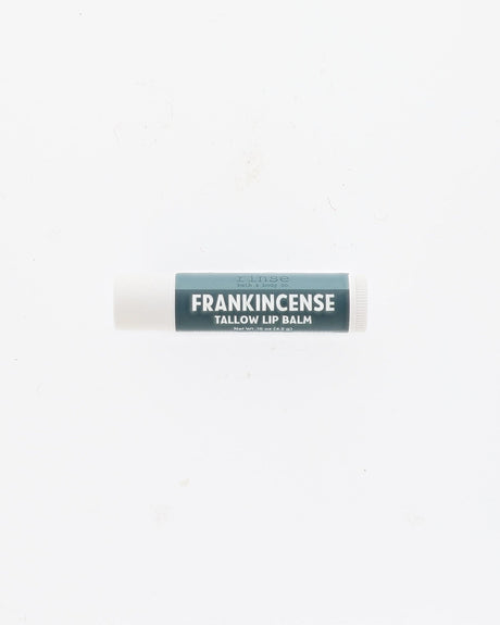 Frankincense Tallow Lip Balm tube with deep teal label and white cap lying on a plain white background
