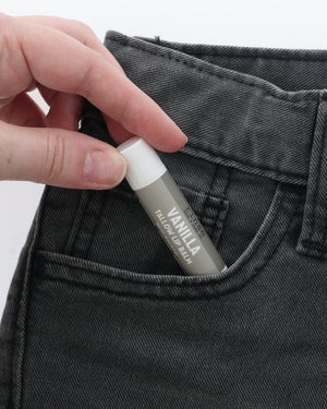 Vanilla Tallow Lip Balm half-tucked into the front pocket of charcoal jeans, held between two fingers